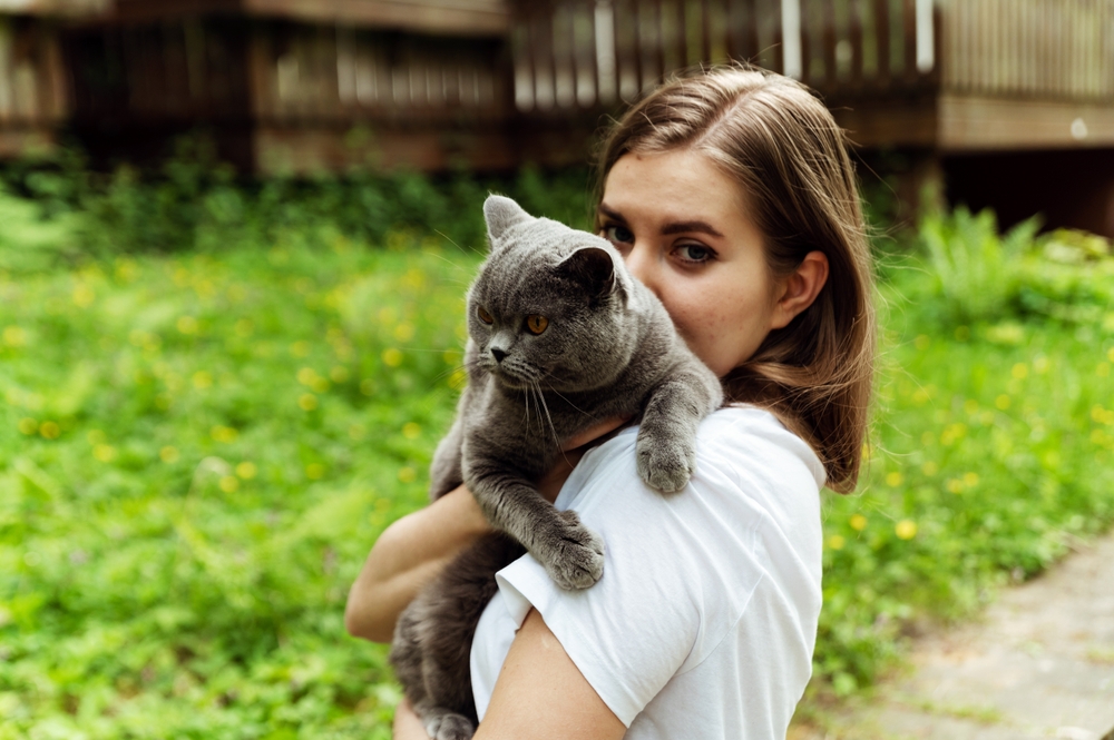 young girl hugging a grey cat outside